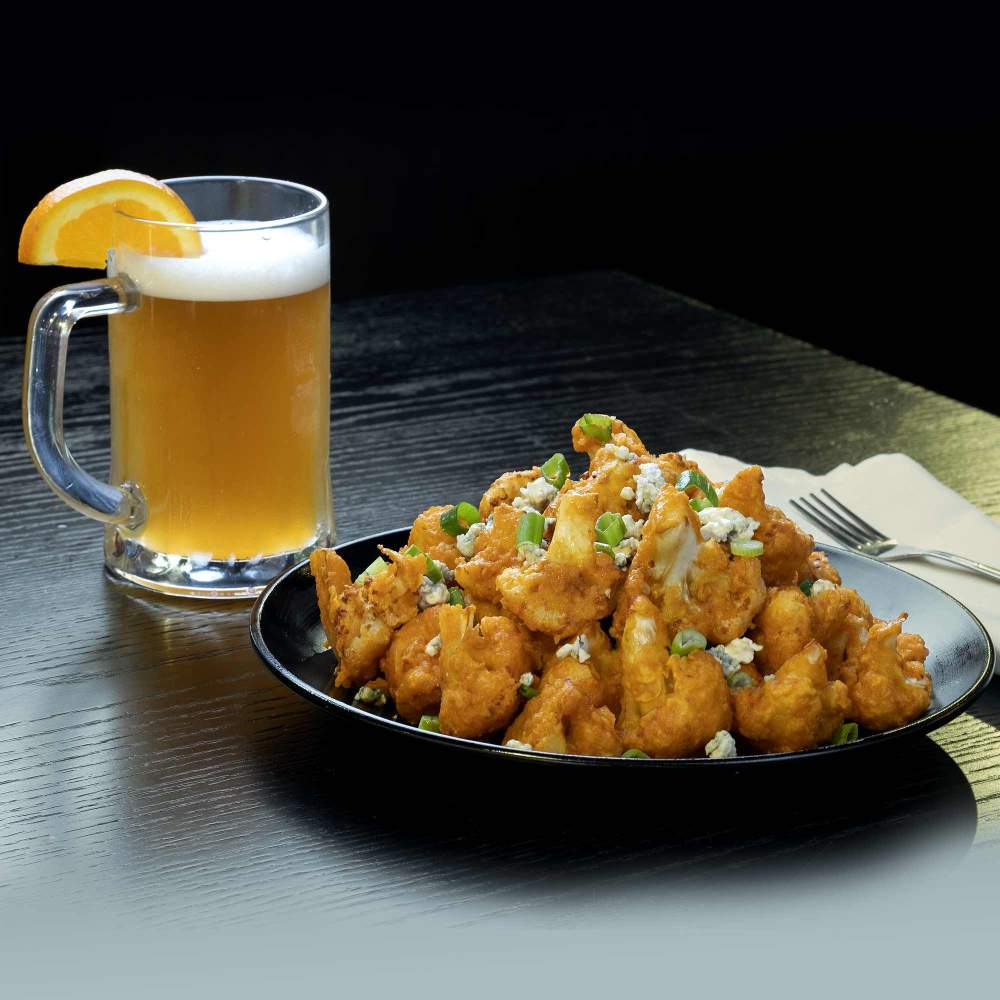 a plate of fried cauliflower next to a glass of beer