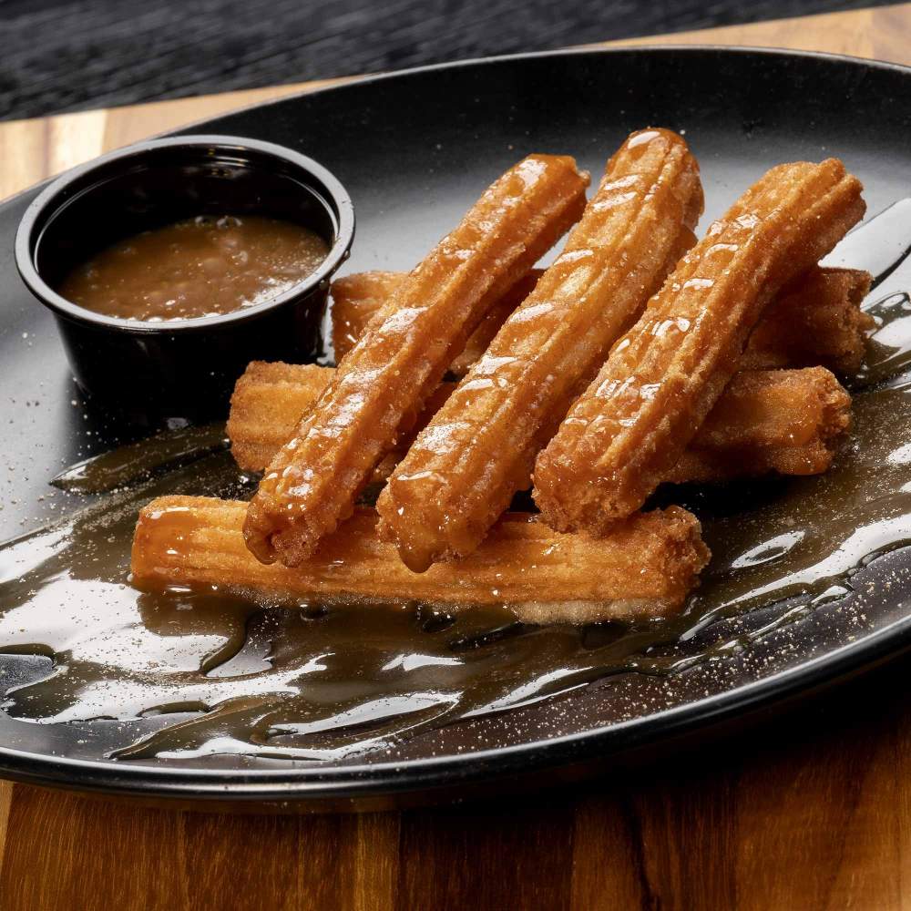 a  plate containing six churros and a bowl of sauce
