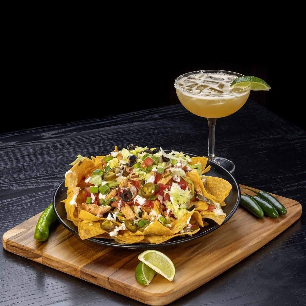 a plate of nachos and a cocktail with a slice of lime on the rim on a table